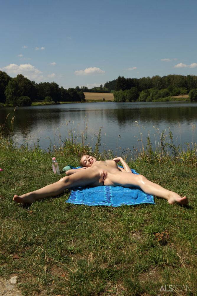 Tiny teen pegs her pink twat while naked on a towel by a river | Photo: 1579032