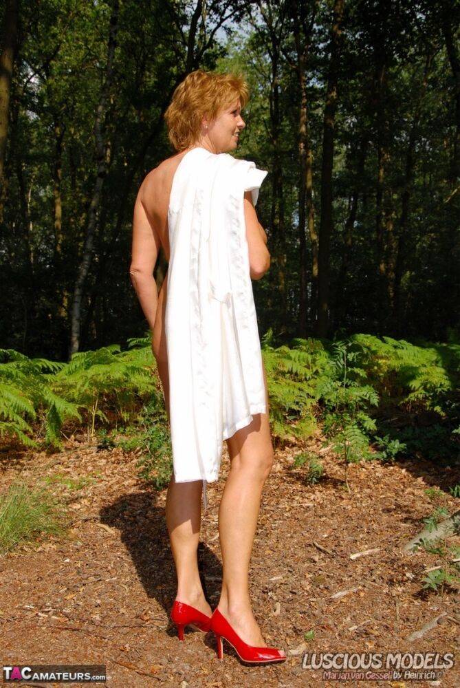 Older redhead removes a robe to stand naked in red heels while in the woods - #1