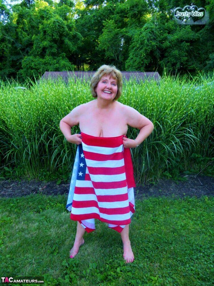 Older plumper Busty Bliss holds an American flag while totally naked in a yard - #11