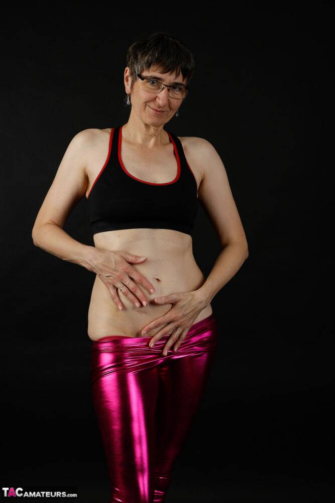 Mature woman models a sports bra in shiny pants and black boots - #4