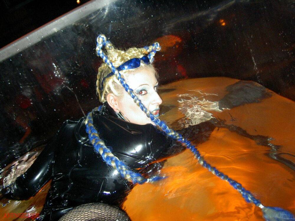 Caucasian female Dark Wing models latex apparel while in a watery cage - #10