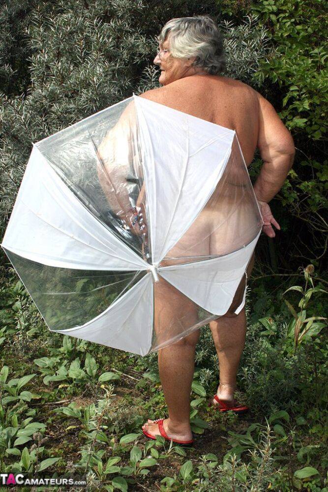 Obese oma Grandma Libby holds an umbrella while posing naked by fir trees - #5