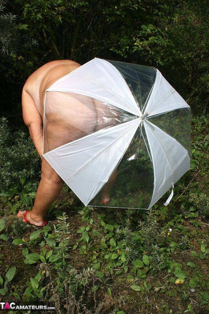 Obese oma Grandma Libby holds an umbrella while posing naked by fir trees - #1