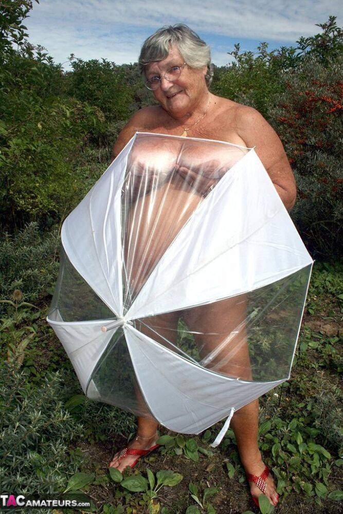 Obese oma Grandma Libby holds an umbrella while posing naked by fir trees - #7