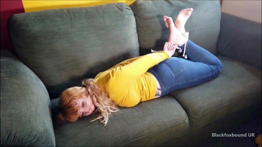 Barefoot white girl is hogtied on a sofa while ball gagged in her clothing - #5