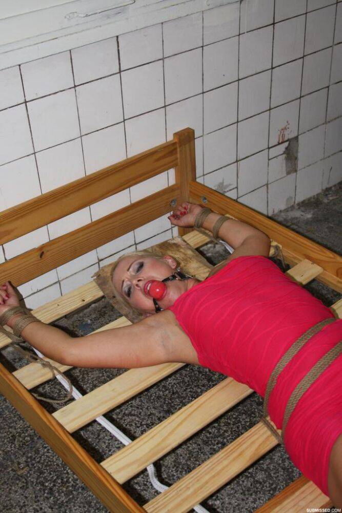 Ball gagged blond female struggles against rope restraints with dress hiked up - #1