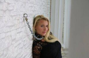 Fully clothed blonde is fastened to a wall with chains in handcuffs on picsofsex.com