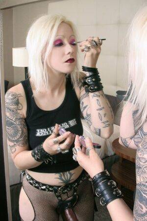 Tattooed blonde rocker Cindy B does her makeup while wearing a strapon cock on picsofsex.com