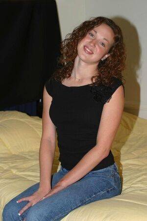 Amateur model with curly red hair finger spreads her pierced pussy atop a bed on picsofsex.com