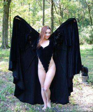 Redhead amateur Amber Lily models nude in a forest draped in a black cape on picsofsex.com