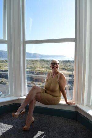 Big titted older woman Barby Slut showcases her bald twat in front of a window on picsofsex.com
