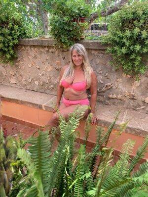 Older blonde Sweet Susi removes a pink bra and panty set to go nude in garden on picsofsex.com