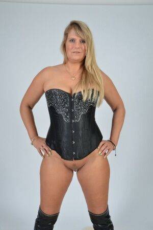 Mature blonde Sweet Susi displays her trimmed pussy in a corset and OTK boots on picsofsex.com