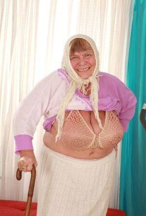 Old granny Sara G in skirt & boots sheds sweater to show huge tits in bra on picsofsex.com