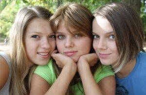 Three young looking girls gets naked on a wooden bench in the countryside on picsofsex.com