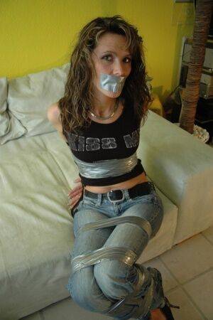 Clothed female is silenced and restrained with duct tape on a sofa on picsofsex.com