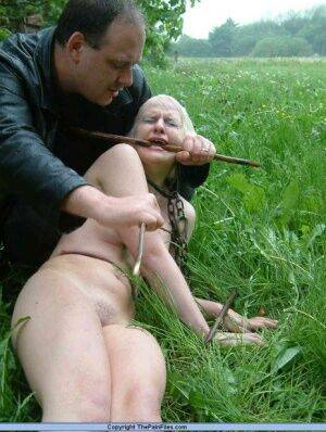 Naked blonde slave is caned and stomped on in a field of lush grass on picsofsex.com