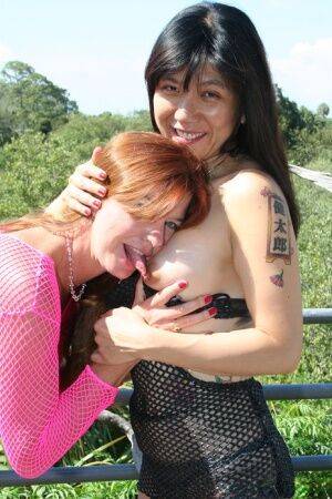 Mature redhead Dee Delmar and a tattooed girl blow a black dick together on picsofsex.com