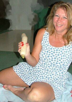 Mature amateur woman Devlynn toys her pussy with a veggie atop a sheet on picsofsex.com