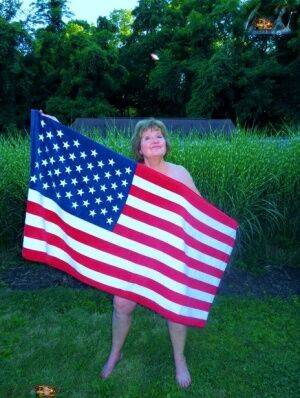 Older plumper Busty Bliss holds an American flag while totally naked in a yard - Usa on picsofsex.com