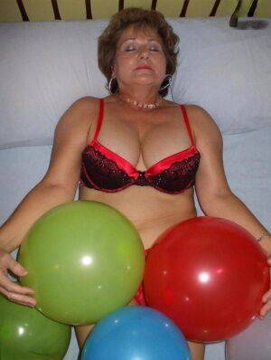 Mature woman Busty Bliss goes topless on her bed while playing with balloons on picsofsex.com