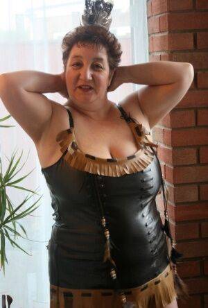 Sick mature woman Kinky Carol models leather lingerie in black boots on picsofsex.com