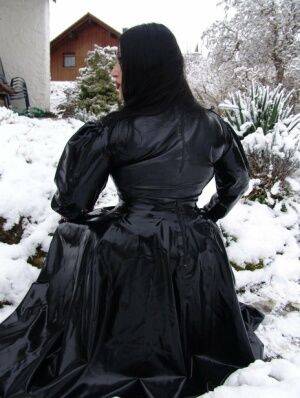 Goth woman Lady Angelina models a black latex dress on snow-covered ground on picsofsex.com