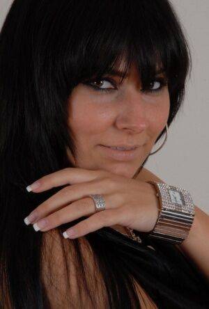 Dark-haired amateur Carie models a large metal watch in a clingy black dress on picsofsex.com