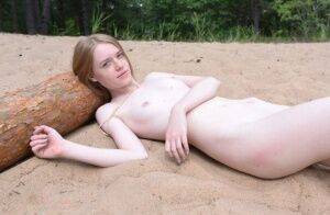 Skinny redhead Gerda models totally naked on a patch of sand in the woods on picsofsex.com