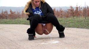 Fully clothed girl Naomi Bennet pulls down her pants to piss on a dirt road on picsofsex.com