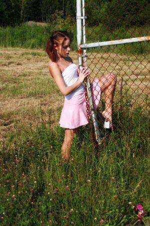 Young redhead Stunning Serena exposes her ass by a chain link fence on picsofsex.com