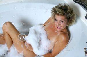 Mature lady soaks in a bathtub while toying her hairy pussy on picsofsex.com