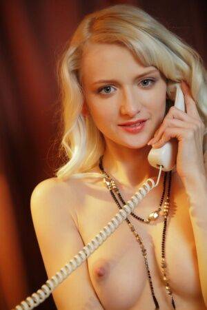 Sweet blonde teen Nika N answers the telephone while wearing a garter belt on picsofsex.com