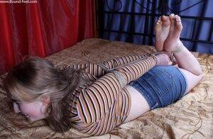 White girl is left on a bed while hogtied in a long sleeved shirt and cutoffs on picsofsex.com