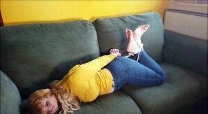 Barefoot white girl is hogtied on a sofa while ball gagged in her clothing on picsofsex.com