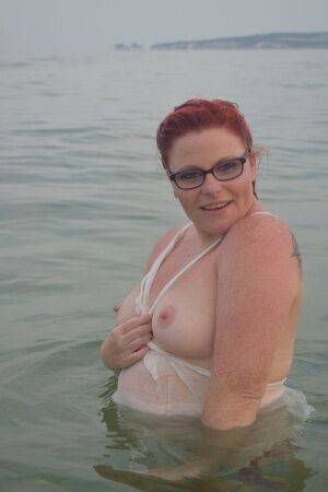 Tattooed redhead poses nude on a beach before masturbating on a toilet seat on picsofsex.com