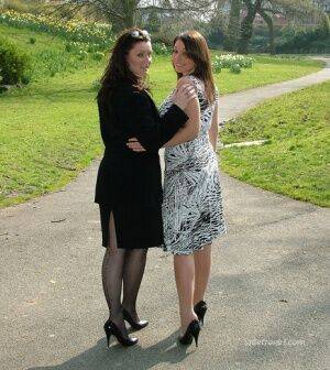 Clothed ladies hold hands while showing their spiked heels on a walking path on picsofsex.com